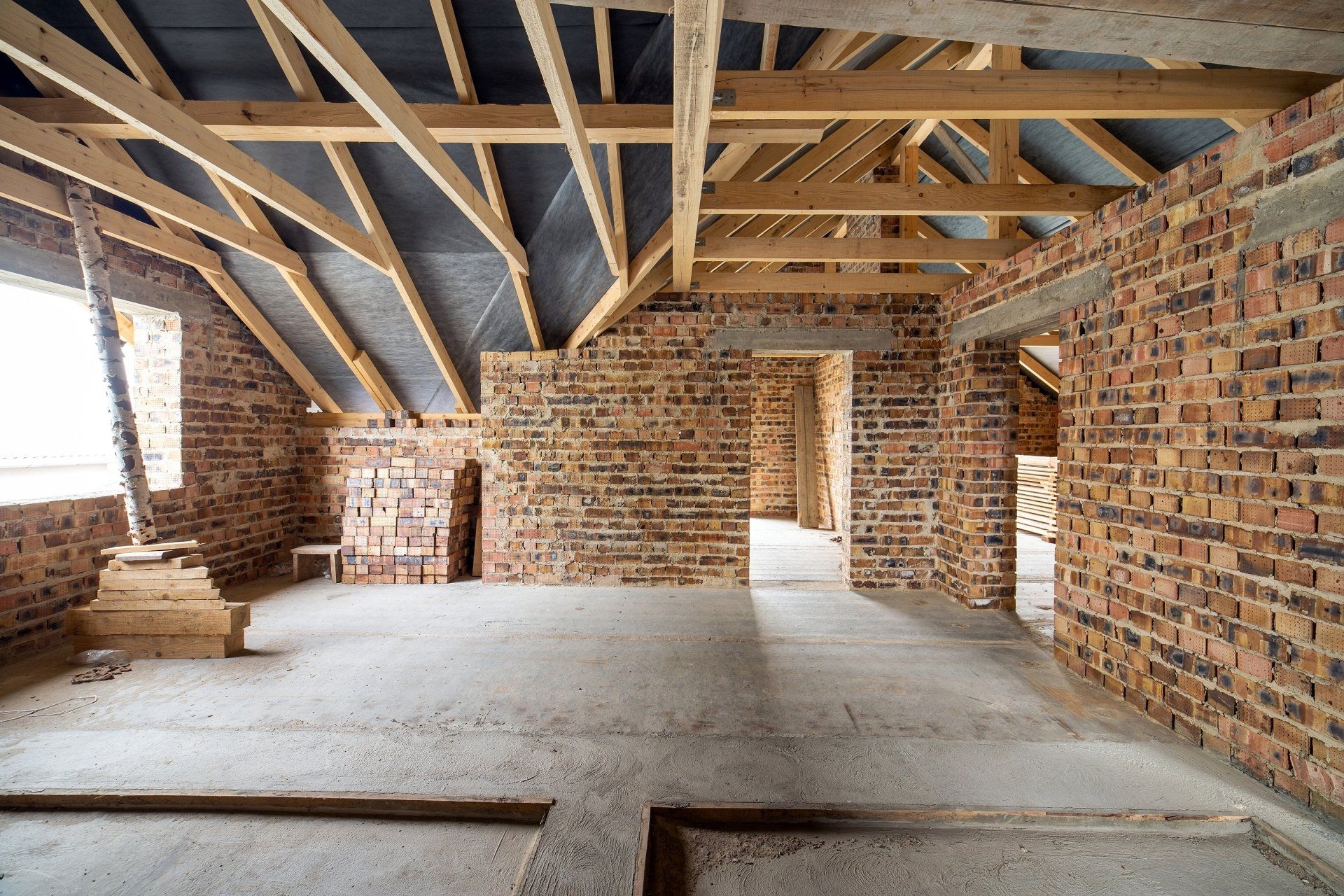 Unfinished room with exposed brick walls, timber roof trusses, and a bare concrete floor under construction