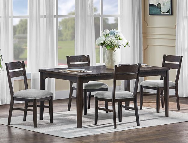 Dark wood dining table with six chairs in a bright room by large windows, set with a vase of flowers
