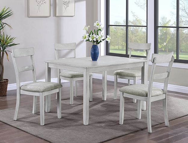 White dining table and chairs in a bright room with a vase of flowers by large windows