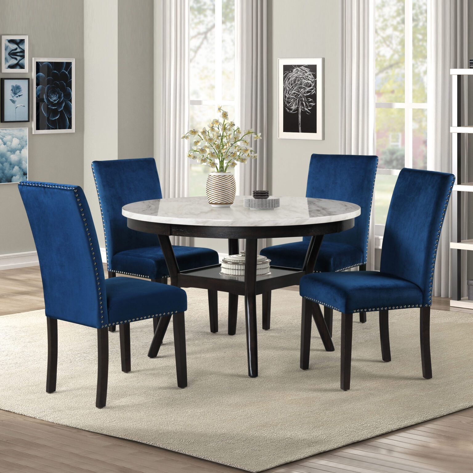 Dining table with four blue upholstered chairs in a bright room with a beige rug and vase centerpiece