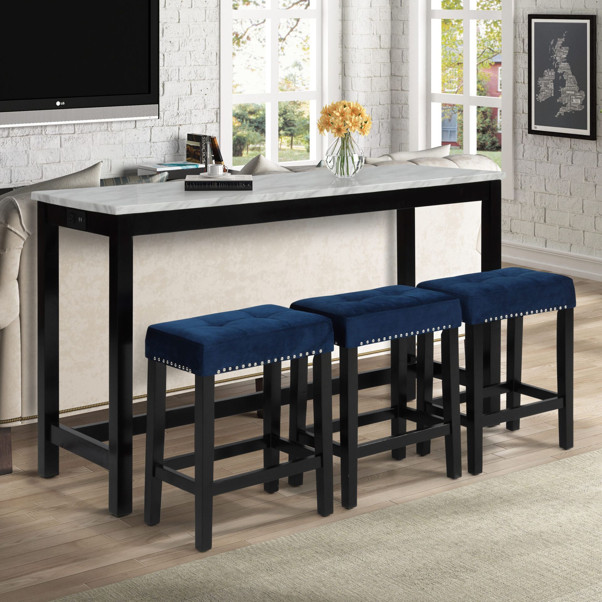 Black kitchen island table with three blue-cushioned stools beside a bright window and white brick wall.
