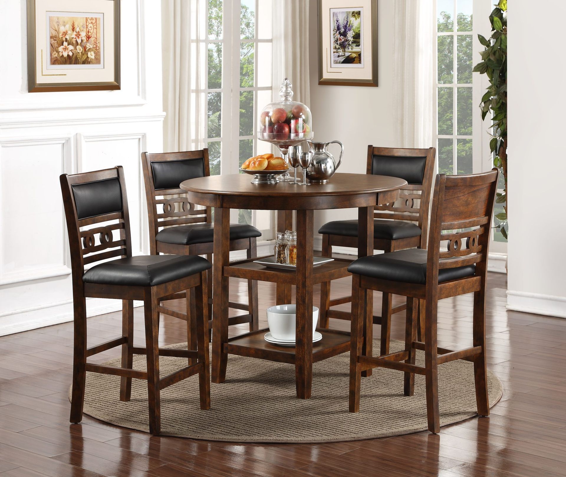 Tall wooden dining table with four chairs on a round rug in a bright room with windows and wall art