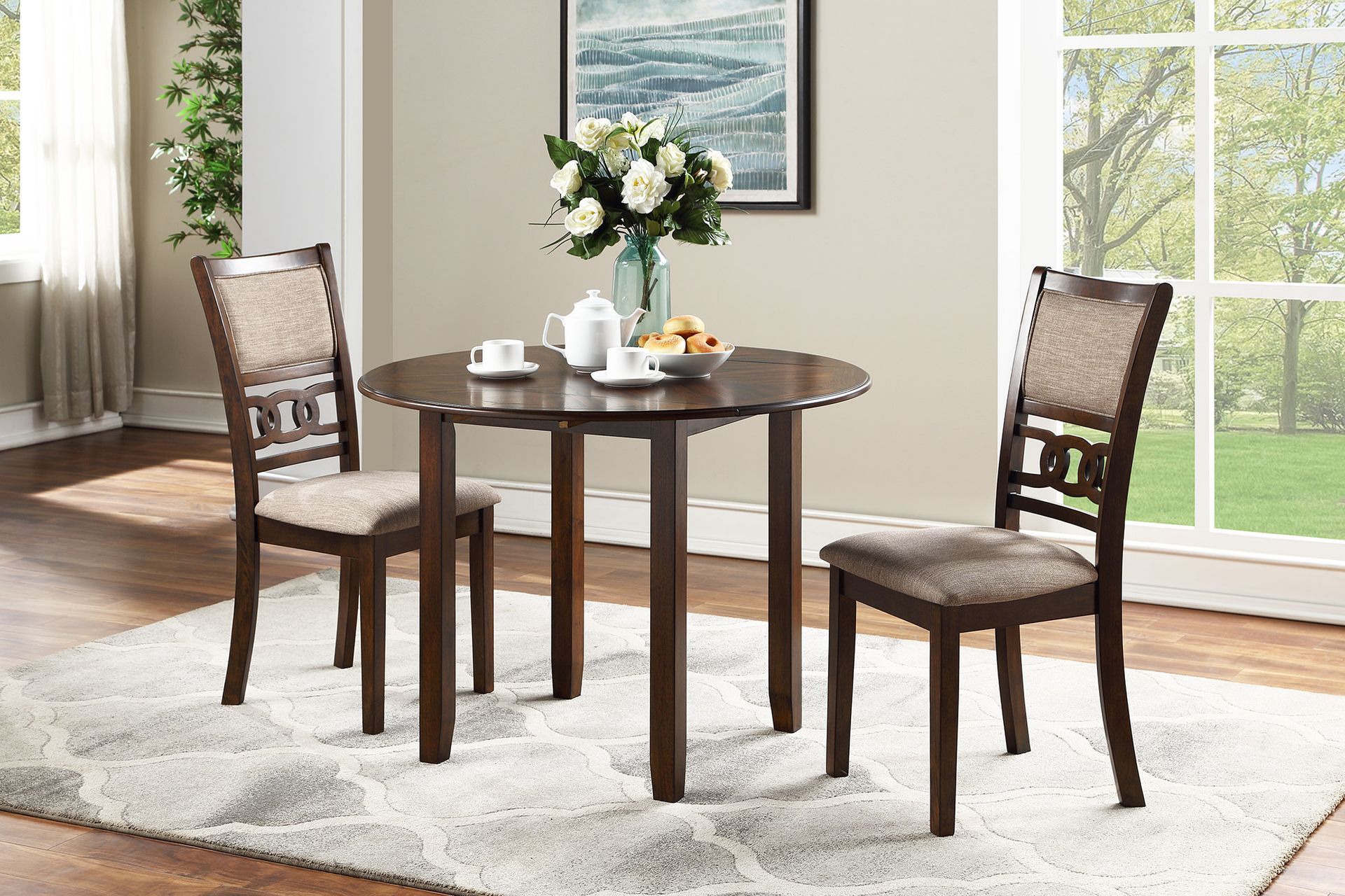 Round wooden dining table with two chairs, flowers, tea set, and fruit in a bright room with large windows