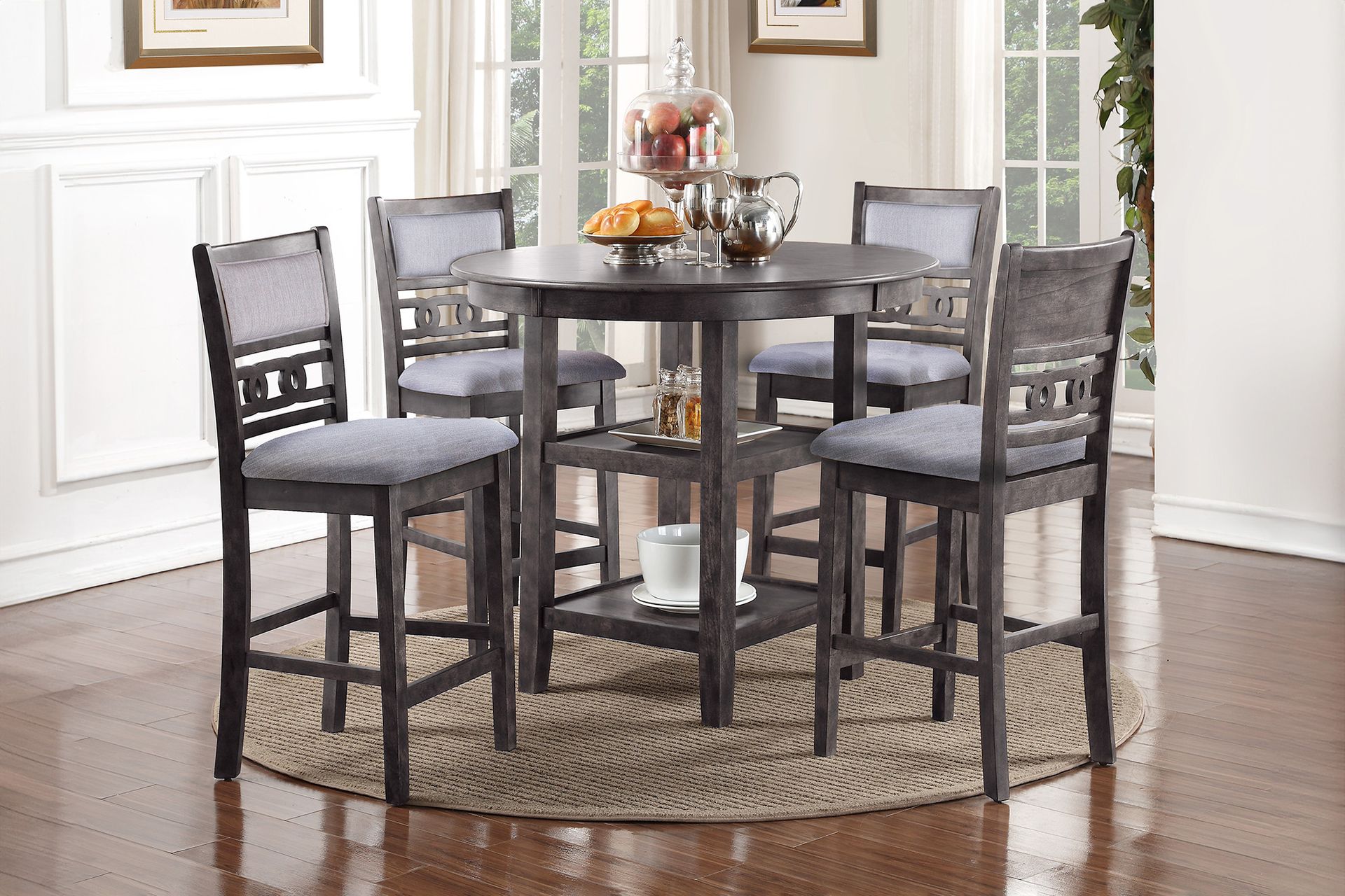 Round dark wood dining table with four chairs on a woven rug in a bright dining room