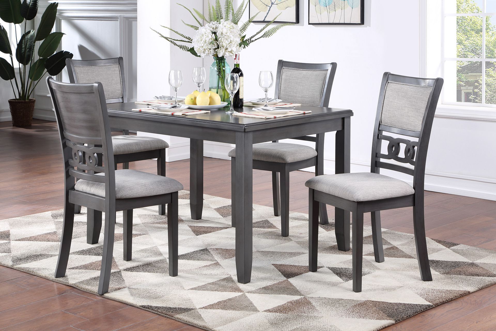 Gray dining table with four chairs on a patterned rug in a bright dining room