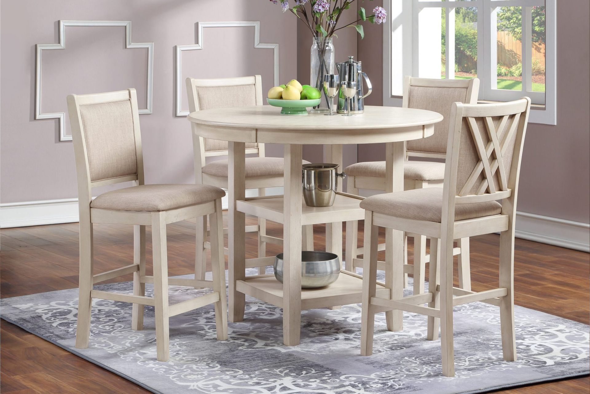 Round white dining table with four beige chairs in a bright room with patterned rug and window light