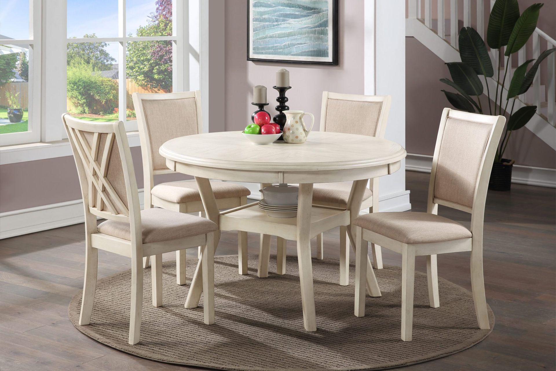Bright dining room with a round white table, four chairs, rug, and large windows with plants.