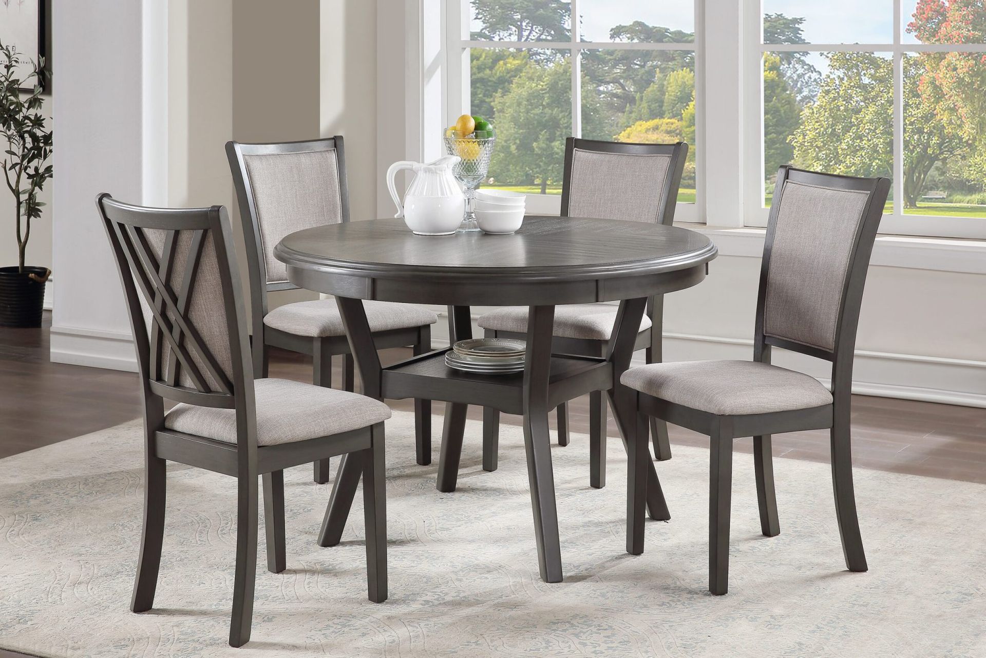 Round dining table with four gray chairs in a bright room by large windows