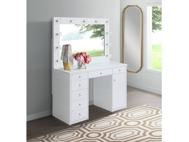 White vanity desk with mirror, drawers, flowers, and stool in a bright bedroom near a patterned rug.