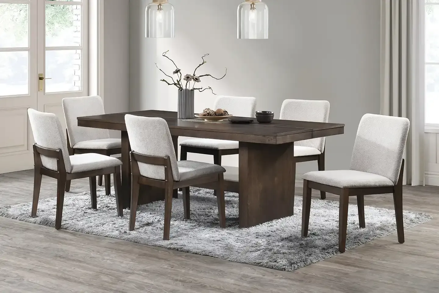 Modern dining room with a dark wood table, white chairs, pendant lights, and a gray rug.