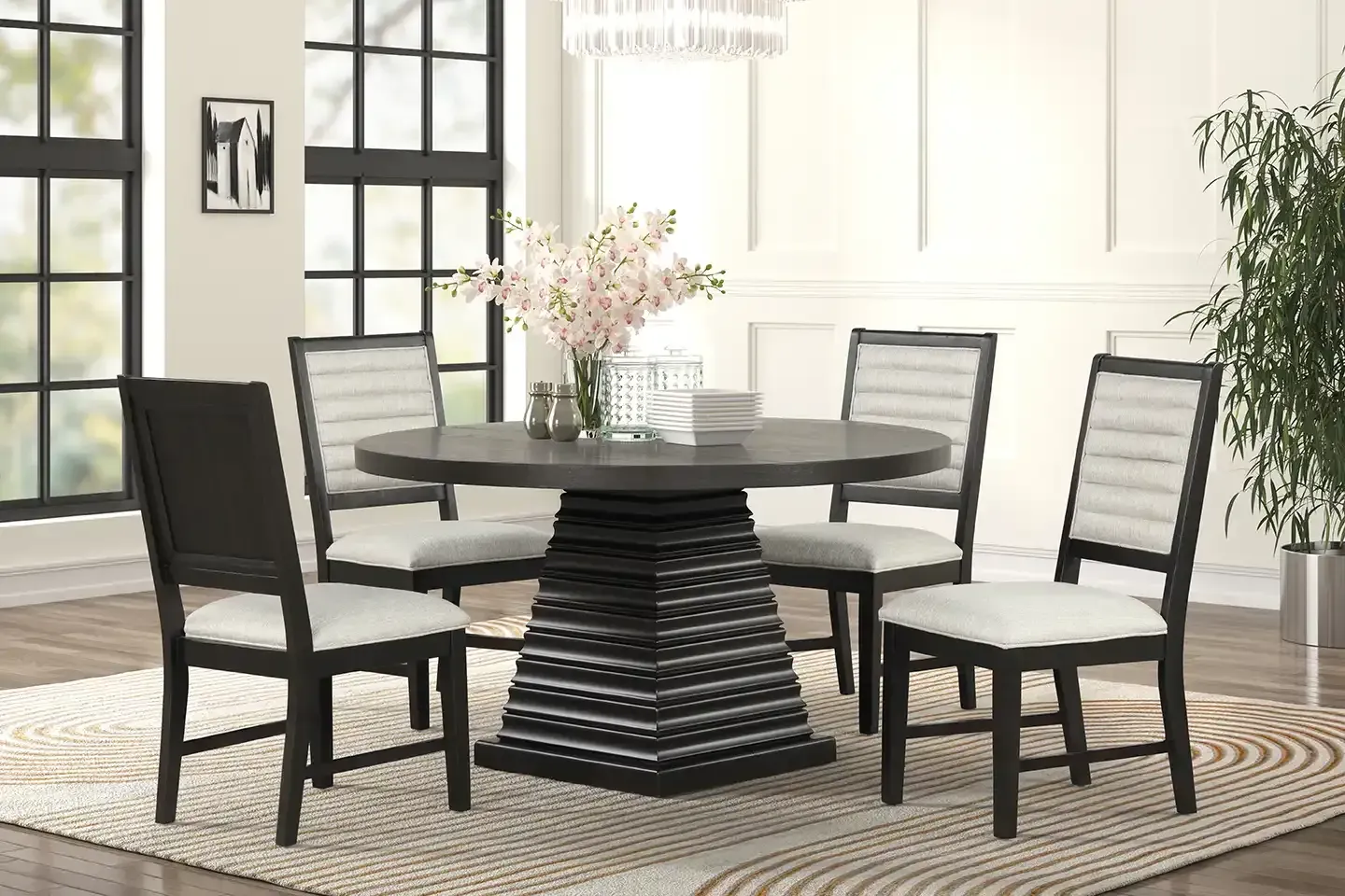Dining room set with round black table, four chairs, and vase of flowers on a patterned rug.