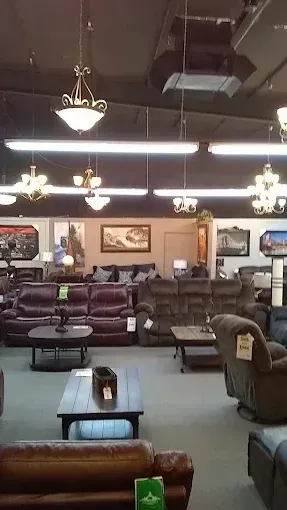 Furniture showroom with sofas, chairs, tables, and hanging lights under a high ceiling.