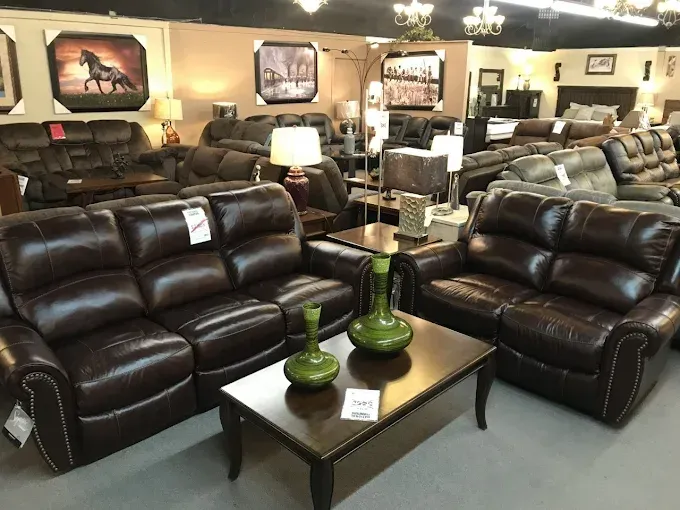 Furniture showroom with dark brown leather sofas and a glass coffee table with green vases.