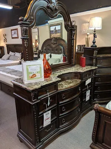 Ornate dark wood dresser with mirror, lamp, and decor in a furniture showroom.