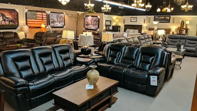 Furniture showroom with black leather sofas, coffee tables, lamps, and framed decor