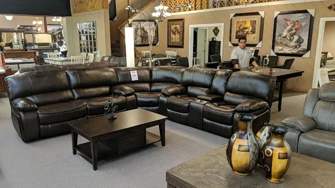 Furniture showroom with a dark leather sectional, coffee table, and decorative vases in the foreground