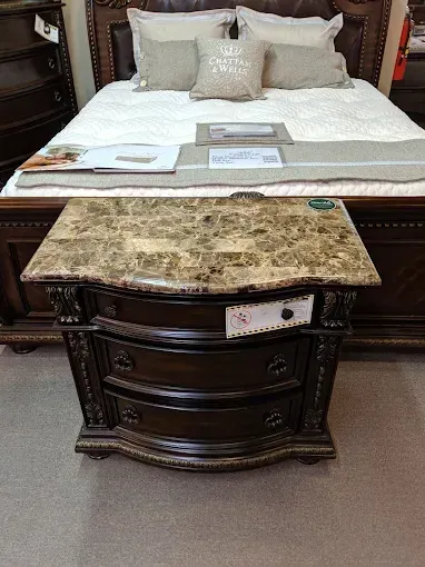 Dark wood nightstand with marble top in front of a bed with white bedding and beige pillows.