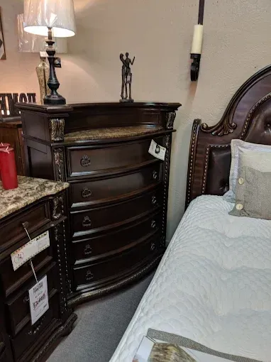 Dark wood dresser beside a bed in a bedroom, with a lamp, granite countertop, and decorative items.