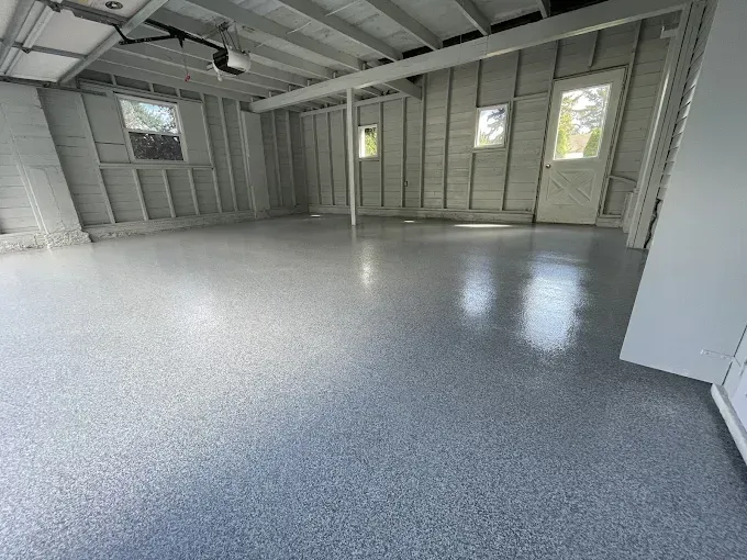 A newly painted garage with a shiny, speckled epoxy floor. Walls are white with small windows.