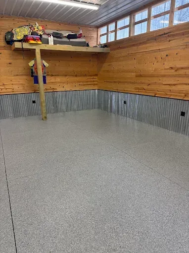 Garage interior with wood-paneled walls, corrugated metal wainscoting, and a speckled gray floor.