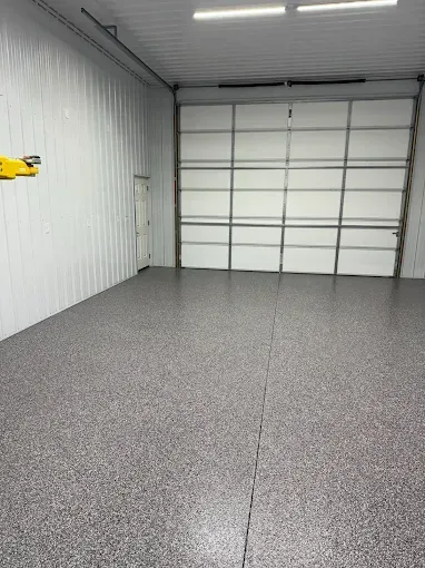 Empty garage interior with a gray epoxy floor, white walls, and a closed overhead door.
