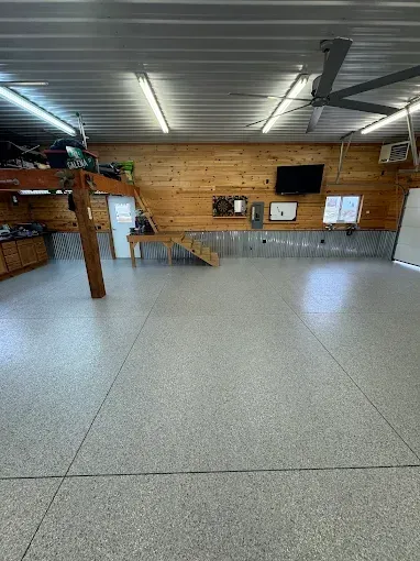 Spacious garage with gray speckled floor, wood-paneled walls, a loft, and a ceiling fan.