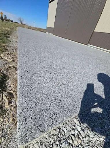 Gray gravel pathway next to a tan building on a sunny day. Shadow of a person taking a photo.