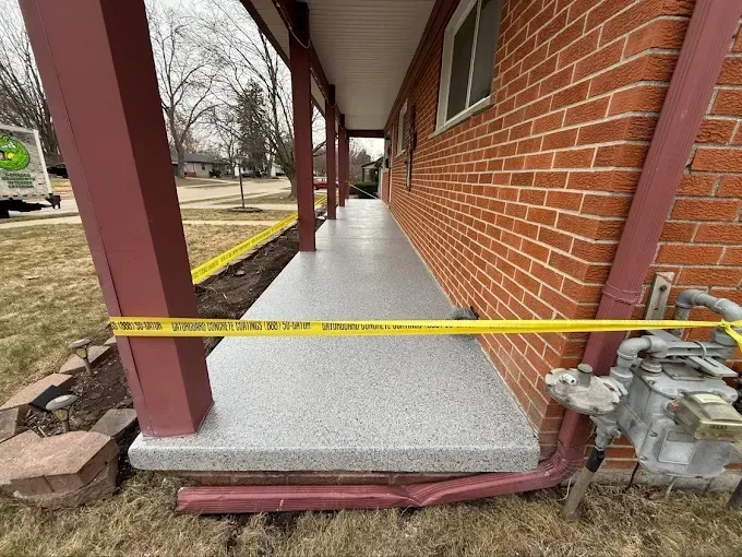 Long, narrow porch with gray speckled flooring, bordered by a brick wall and maroon posts; caution tape present.