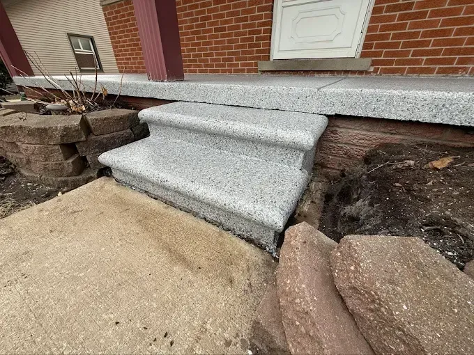 Gray speckled concrete front steps leading to a brick building.