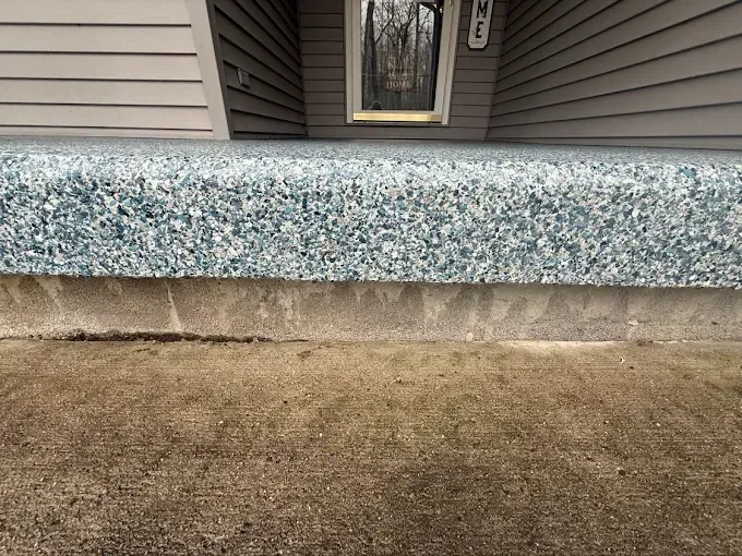 Blue speckled concrete step in front of a house. Brown grass in the foreground, doorway in the background.