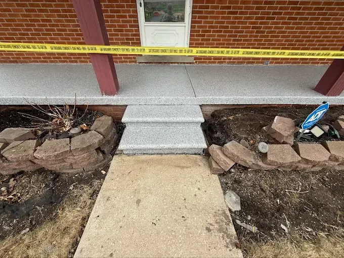 Front porch with steps and caution tape; brown brick, gray concrete, and a small garden.