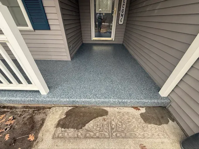 Blue speckled epoxy floor on a front porch with white railing, gray siding, and a welcome mat.