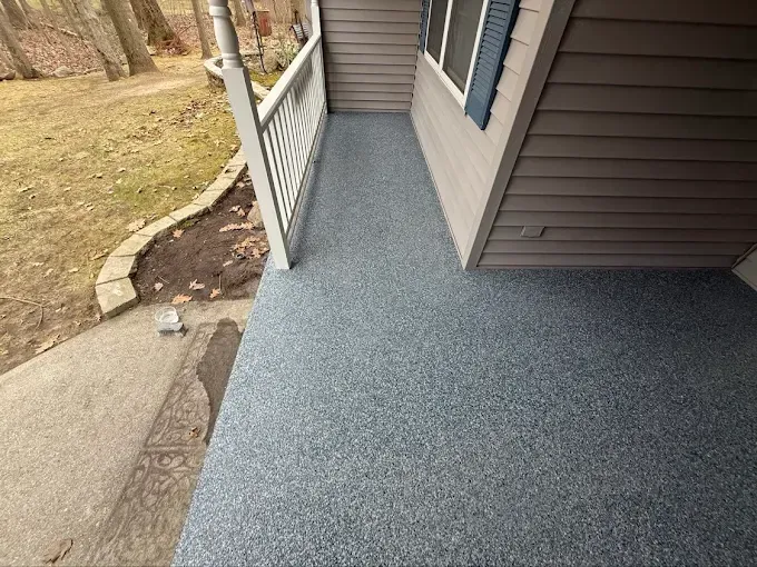 Gray speckled porch floor with a white railing and brown siding.