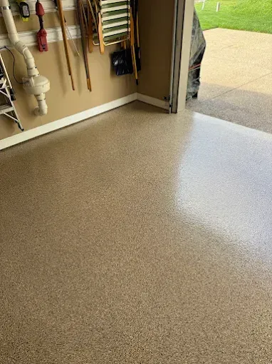 Garage interior with a speckled, tan-colored floor. Tools and a ladder hang on the wall.