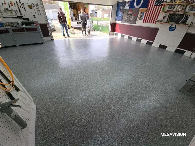 Garage interior with shiny gray floor. Two people stand in the open doorway. Tools and decor are on the walls.