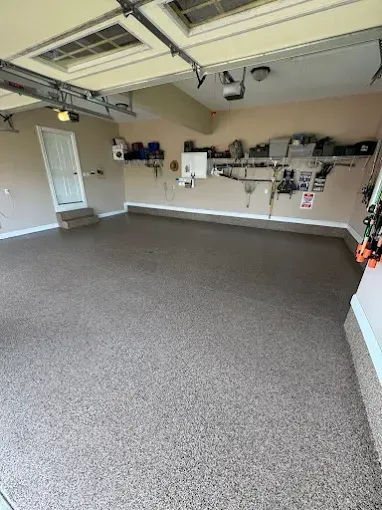 A garage with a speckled floor, beige walls, storage shelves, and a door.