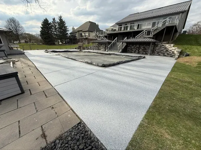 Backyard with a light gray concrete patio, pool cover, and multi-level house.