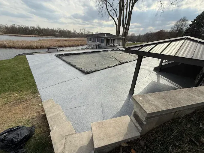 Backyard patio with a pool and covered seating area overlooking a lake.