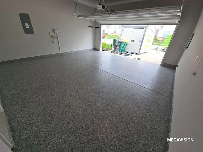Empty garage with gray speckled epoxy floor and open door to outside.