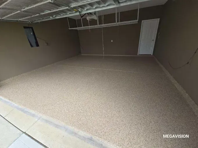 Empty garage with tan speckled flooring, brown walls, white door, and overhead storage.