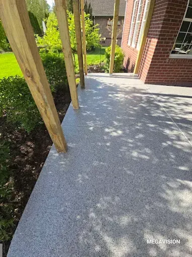 Gray speckled concrete patio with wooden posts, next to a red brick building.
