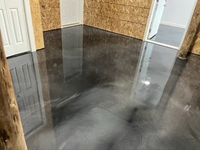 Gray epoxy floor in a room with wood walls, white doors, and a doorway to another room.