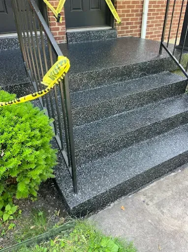 Black speckled concrete steps leading to a dark doorway, with a black railing. Yellow caution tape is visible.