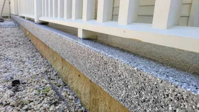 A close-up view of a light-colored speckled concrete base supporting a white wooden porch railing.