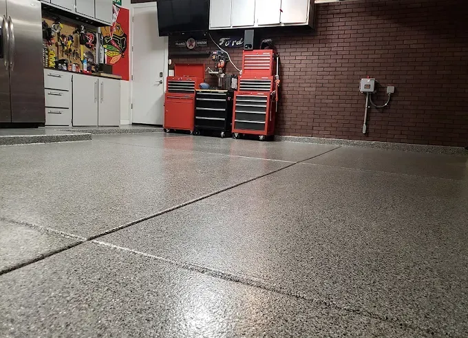 Gray speckled garage floor with red tool chests and white cabinets.