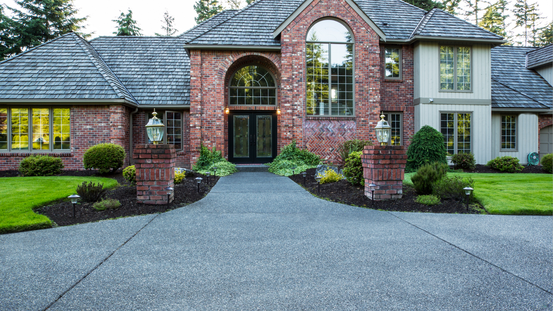 Brick and stucco house with a curved driveway, columns, and a landscaped lawn.