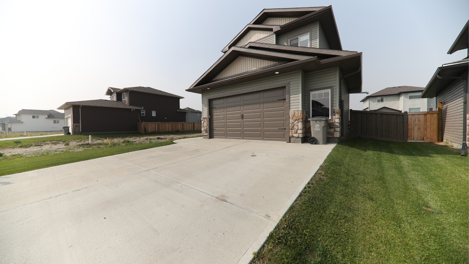 House with brown garage door and driveway; grass in foreground, other houses in the background.