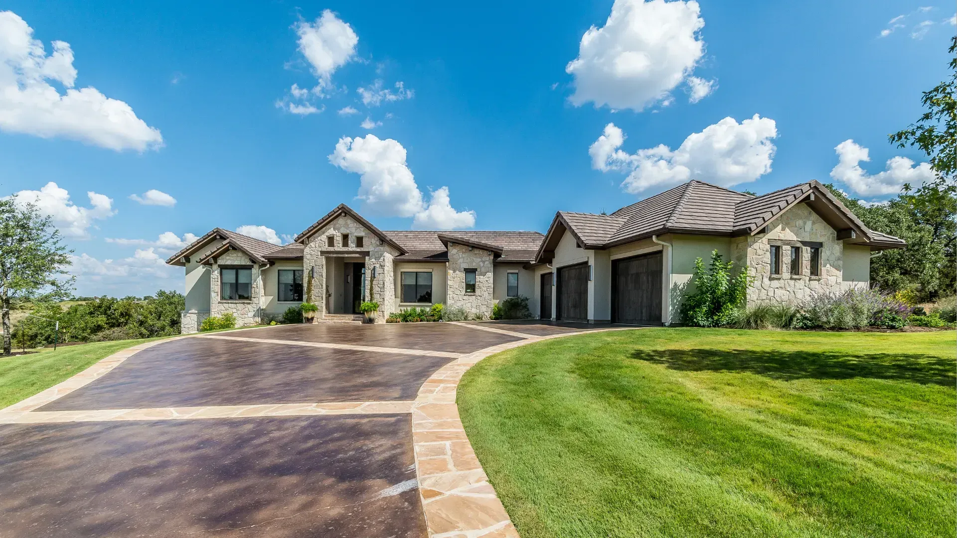 Stone house with a winding driveway and garage on a bright, sunny day.