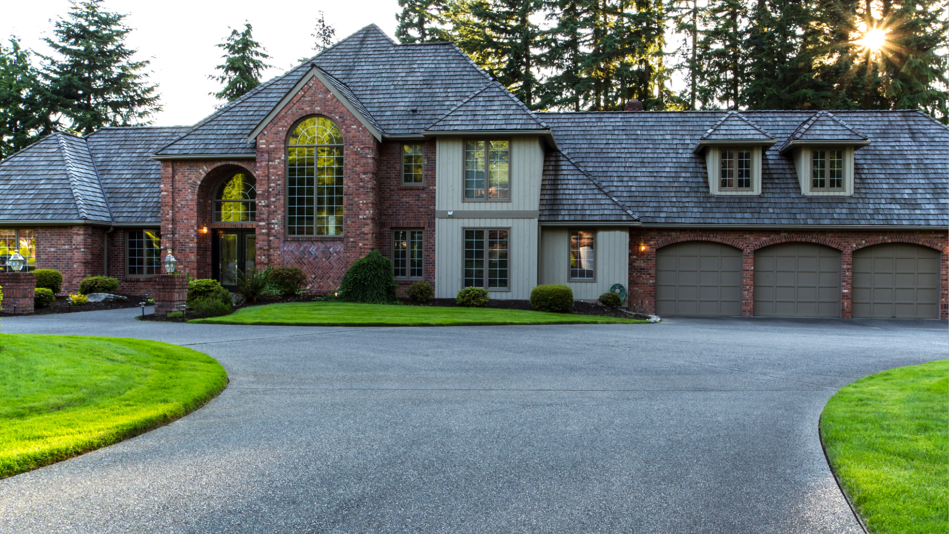 Large brick and gray-sided house with a long driveway and green lawn.