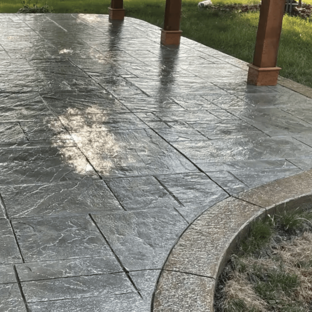 Stamped concrete patio with a curved border, surrounded by grass and supporting wooden columns.